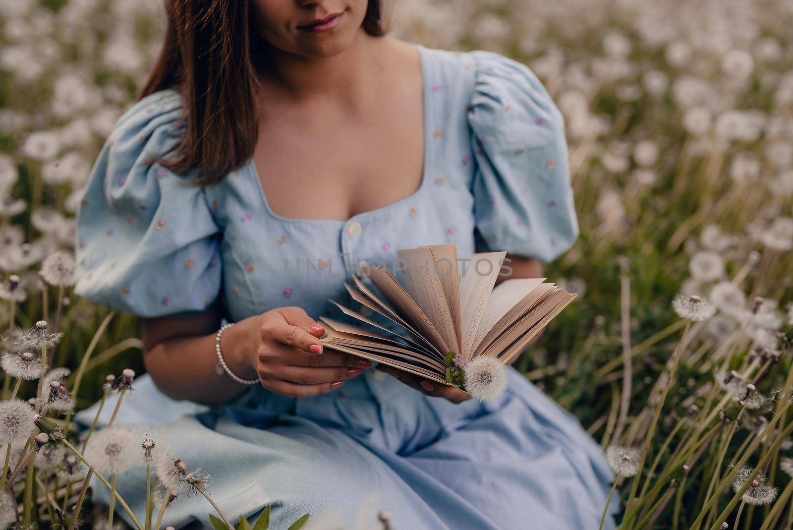 Woman flips through pages of paper book. Lady in retro or vintage dress reading interesting novel while sitting on nature. Atmospheric scene. Education, hobby, entertainment concept.High quality photo