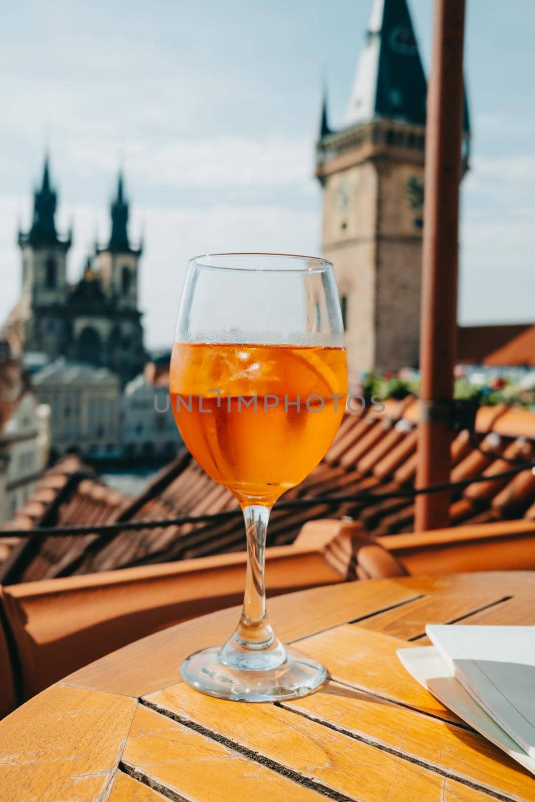Aperol Spritzes cocktail on background of old Prague town square with Church, astronomical clock. Famous historical, gothic style buildings. Sunny cityscape in european capital. High quality photo