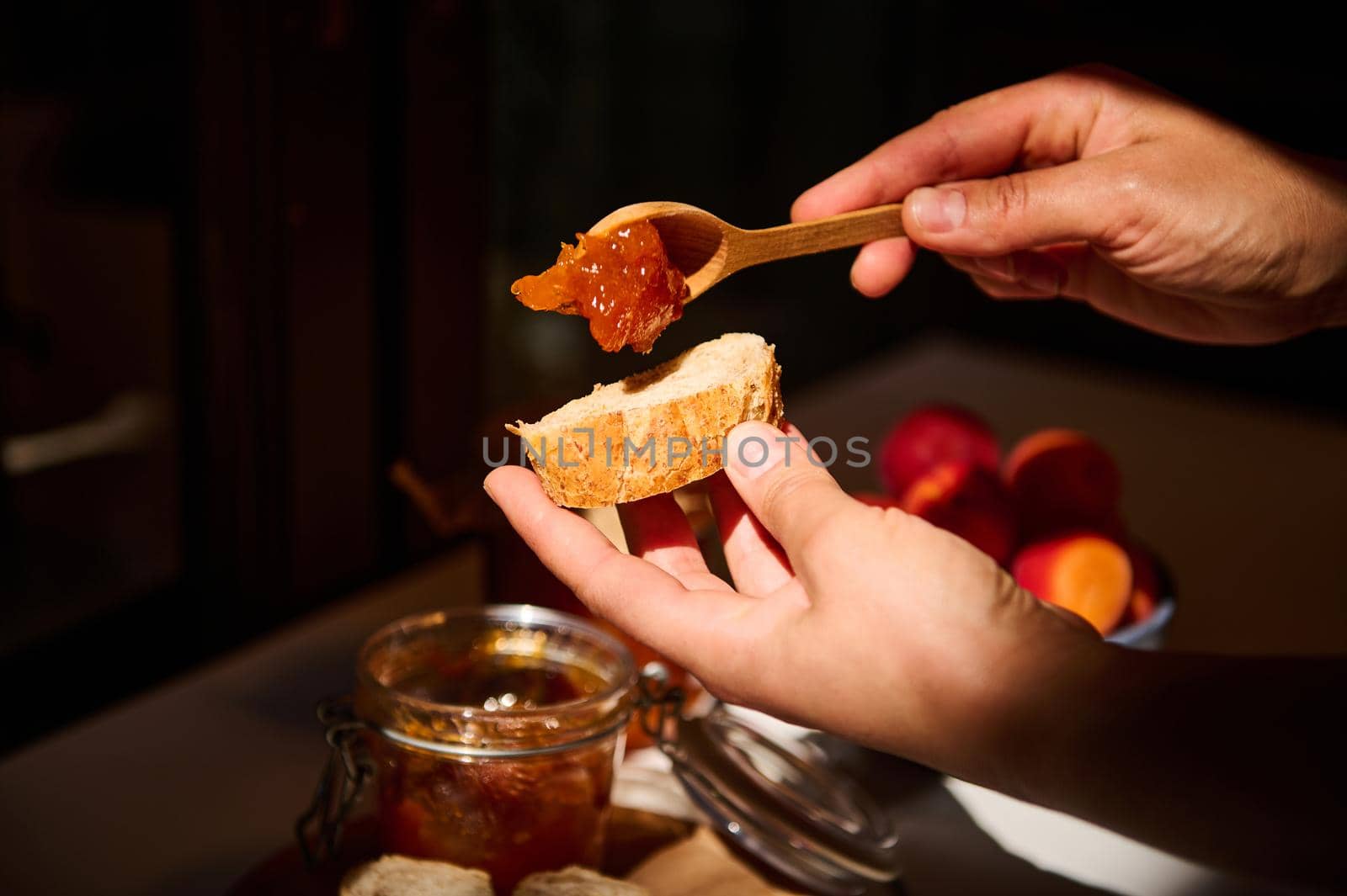 Food and drink, summer autumn harvest concept. Cropped view of hands of housewife holding wooden spoon and spreading homemade apricot jam on bread