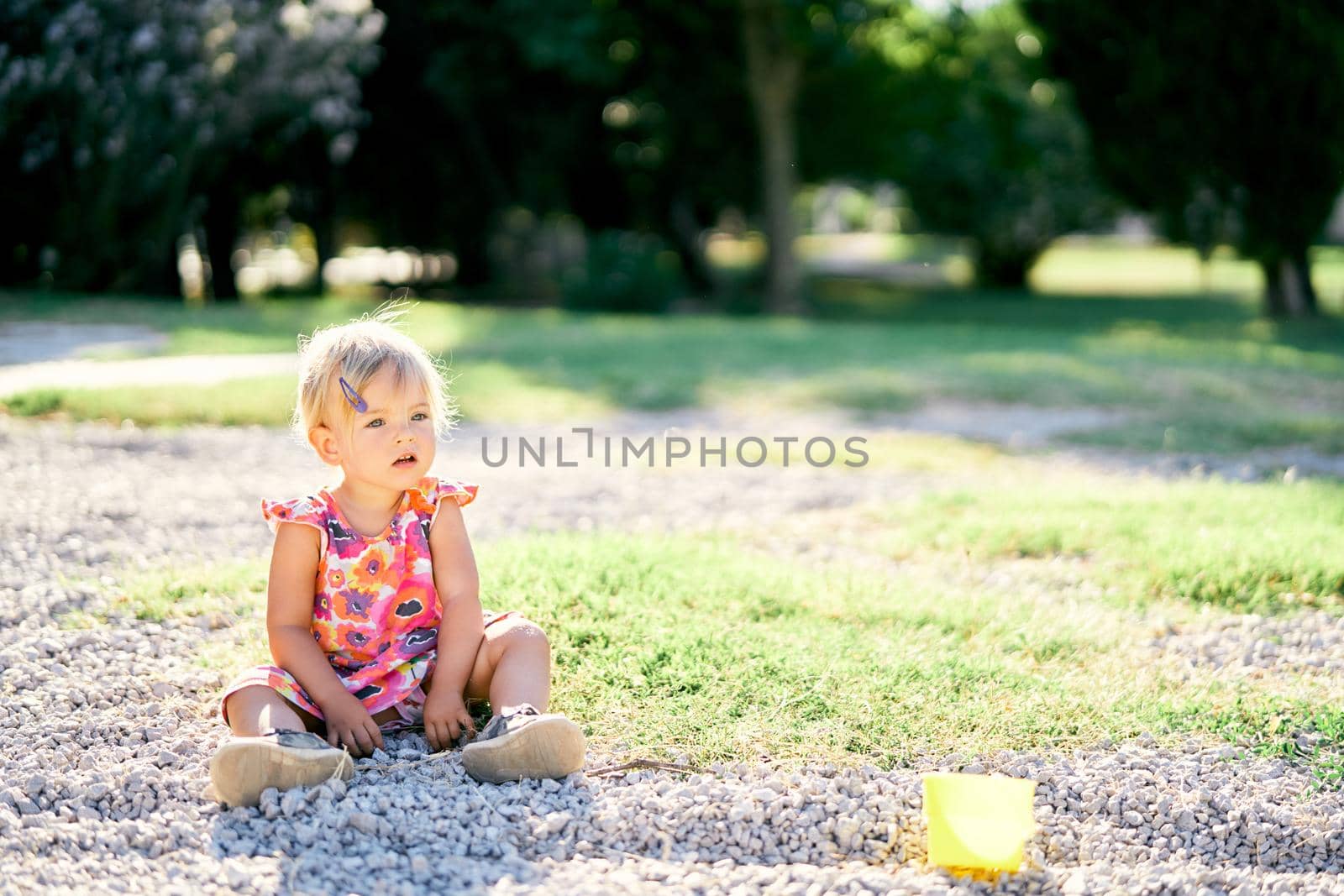 Little girl sits in the park on the pebbles. High quality photo
