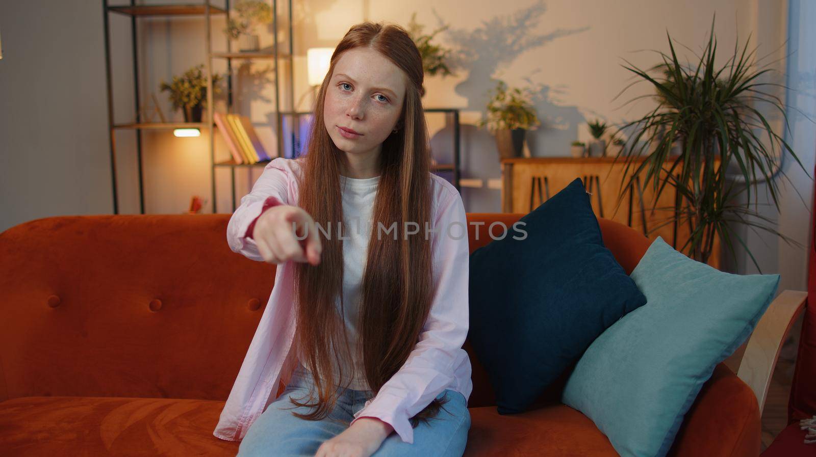 Hey you. Young redhead child girl smiling excitedly and pointing to camera, choosing lucky winner, indicating to awesome you, inviting, approve. Teen freckles kid at home living room sitting on couch