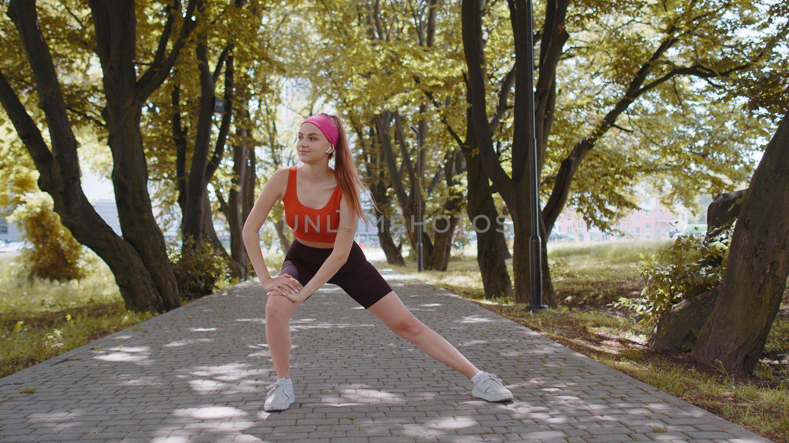 Athletic fit slim sport girl doing squats, listening music in earphones. Fitness workout outdoors in park at morning. Young woman enjoying healthy lifestyle. Active sportswoman. Aerobic, weight loss
