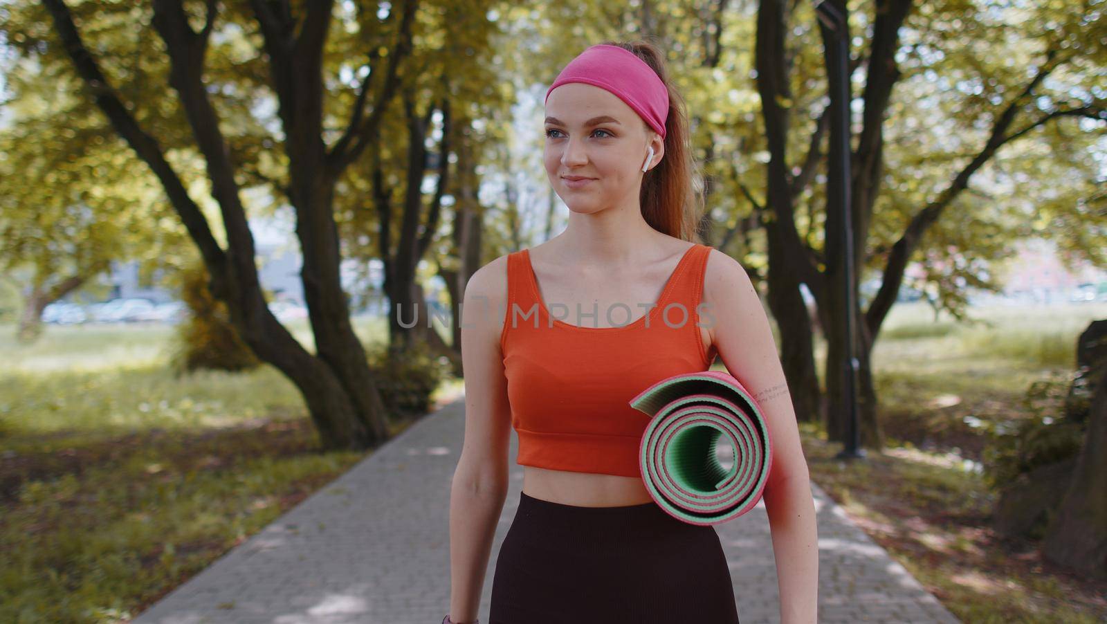 Athletic fitness sport runner girl walking with sport yoga mat to do fitness stretching exercises. Young woman training cardio workout in park at morning. Active sportswoman. Aerobic, weight loss