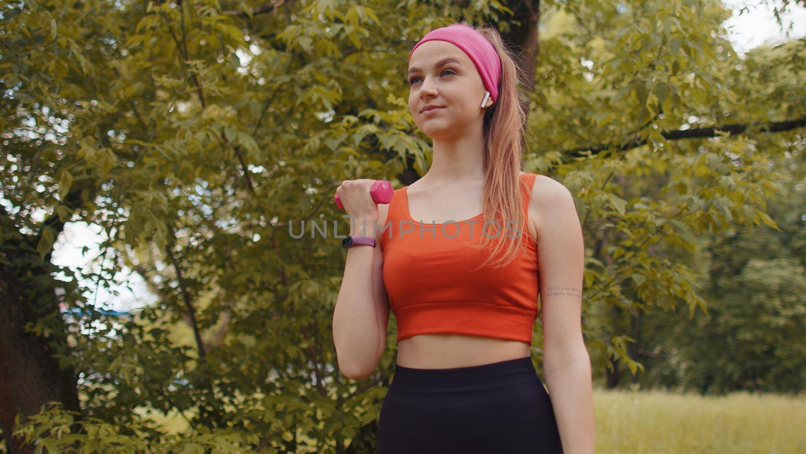 Athletic young sporty fit girl doing dumbbells workout in park performing bicep curls to build arm muscle and strength. Pretty woman enjoying exercising outdoors. Active sportswoman sport motivation