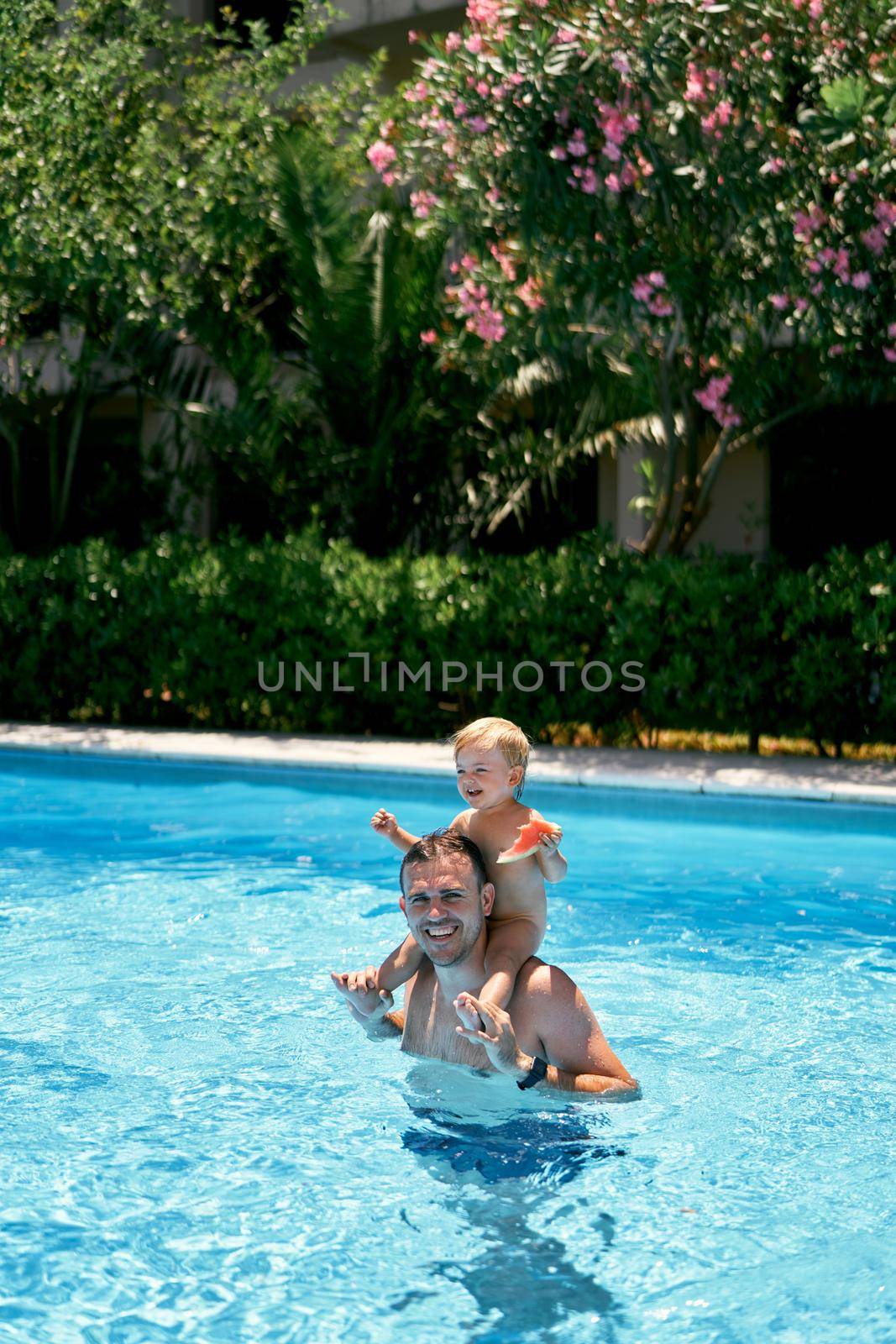 Smiling dad standing in the pool with a small child on his shoulders. High quality photo