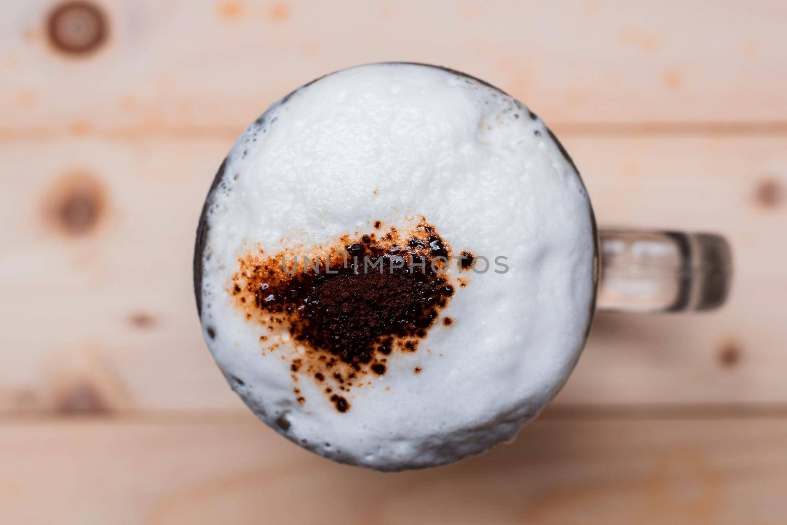 Top view of iced coffee froth in cup and coffee powder with coffee beans on wooden floor.
