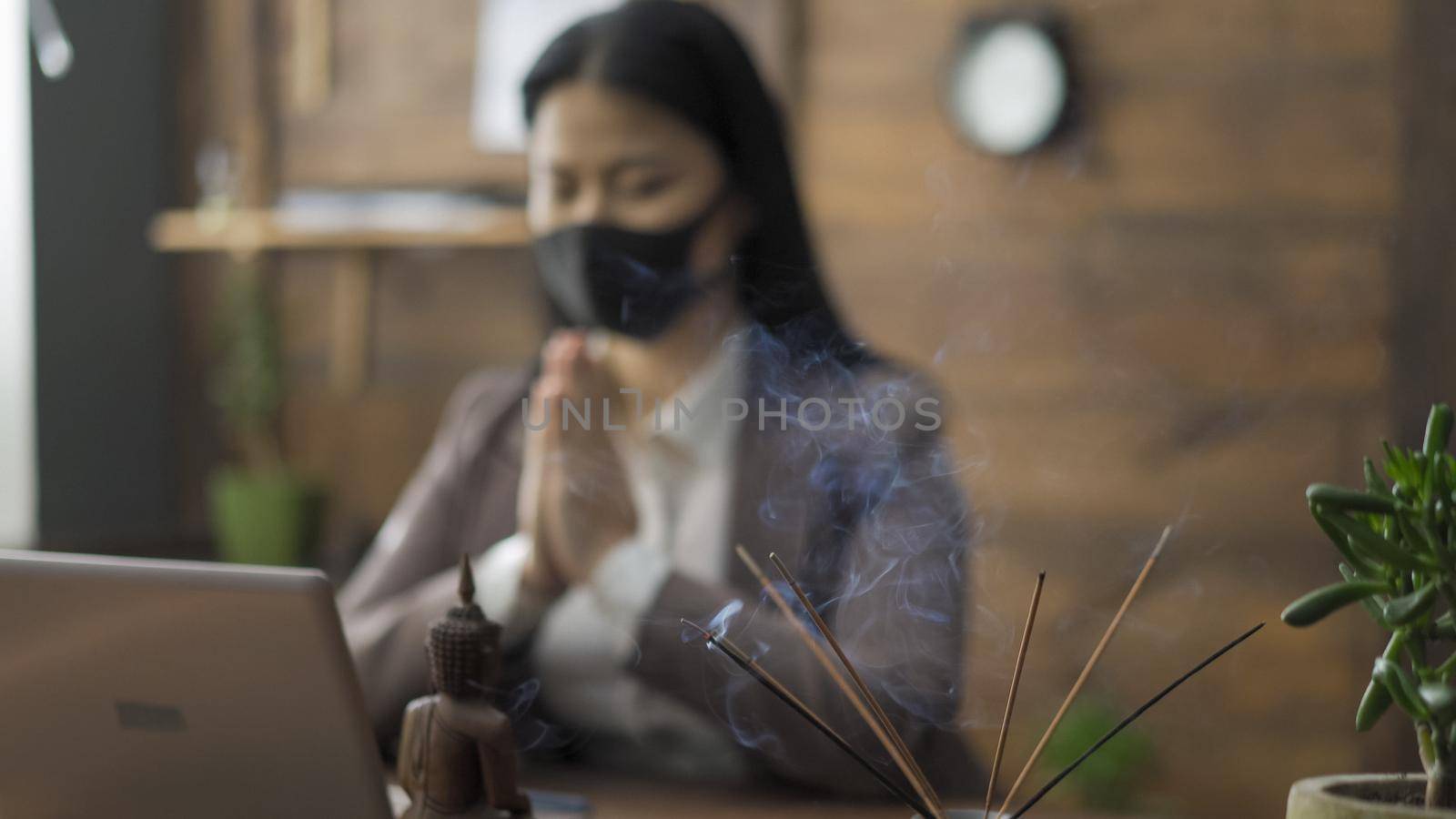 Prayer Of Asian Business Woman Sitting In Mask On Her Face At Office Table In Front Of Laptop, She Clasped Hands Together Reading Prayer, Business During The COVID 19 Pandemic