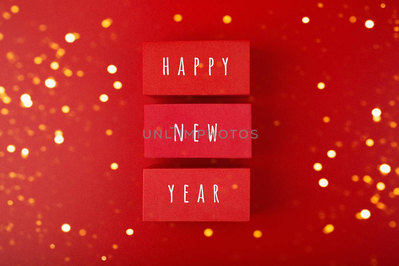 Happy New Year red minimal concept with golden bokeh. Modern flat lay with red toy blocks with written Happy New Year text on red background with golden bokeh. Greeting card for upcoming year