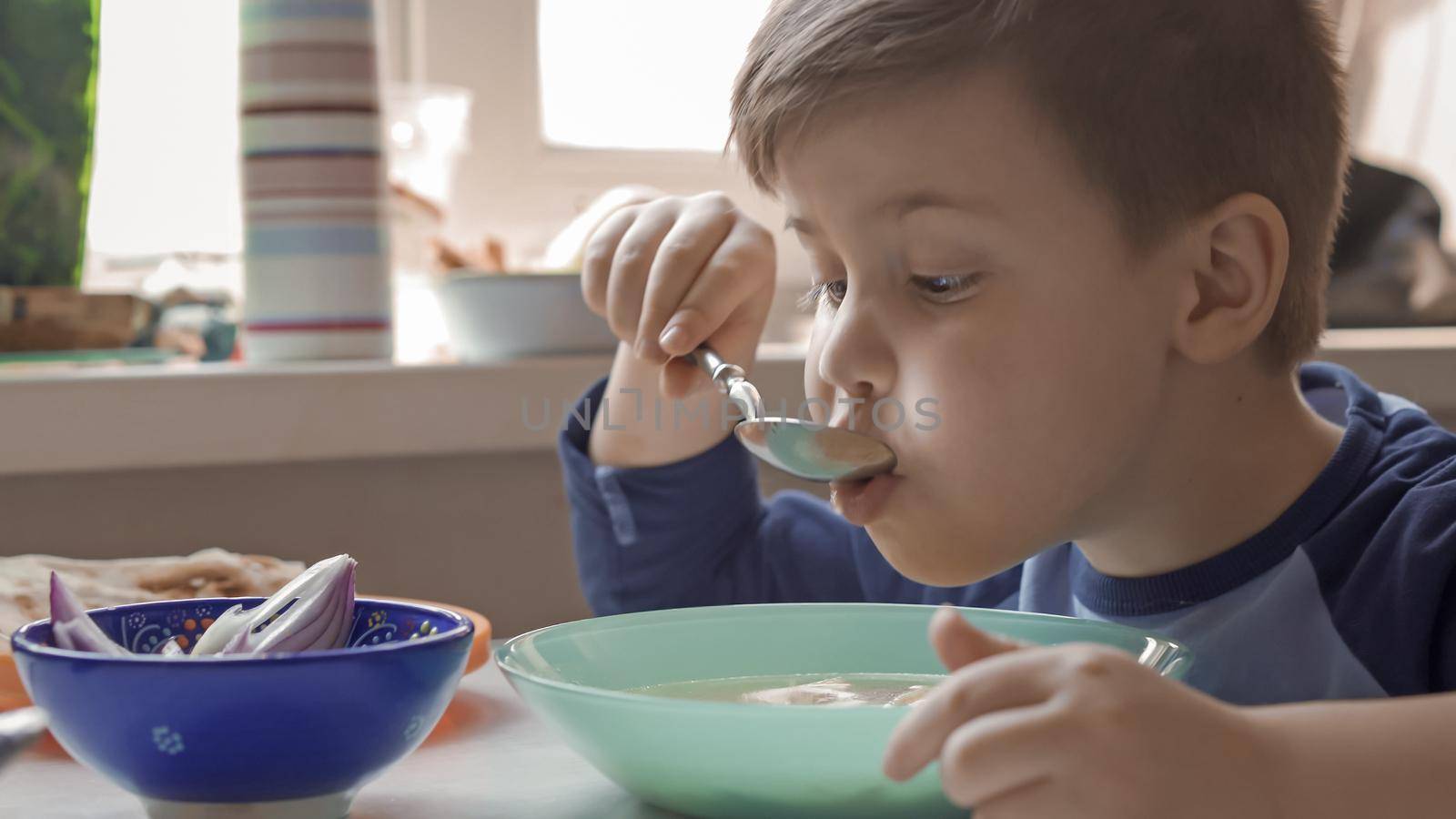 Hungry Boy Eats Soup Sitting At Table In Kitchen, Staying At Home On Quarantine Or Lockdown Days Little Boy Spending More Time With Parents, Preschooler Spend Time Studying At Home, Close Up Shot