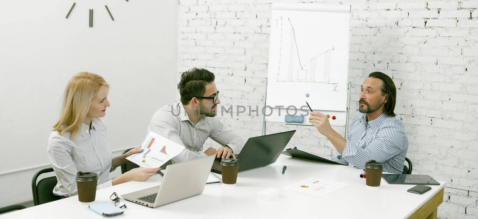 Business team holds a meeting while sitting at a bright office table. Male and female office workers discussing work plans. Toned image.