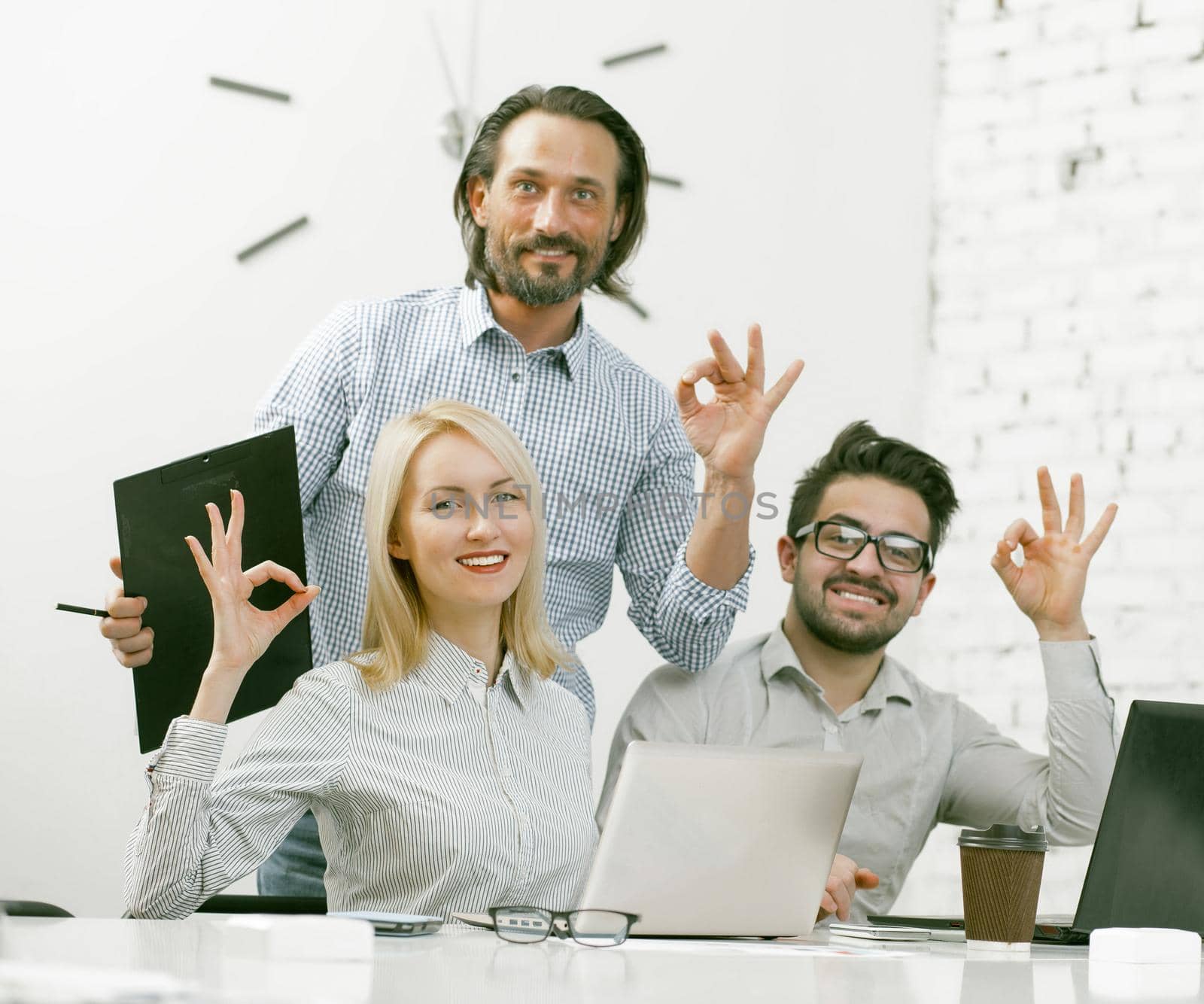 Smiling businessteam showing Ok gestures in office by LipikStockMedia