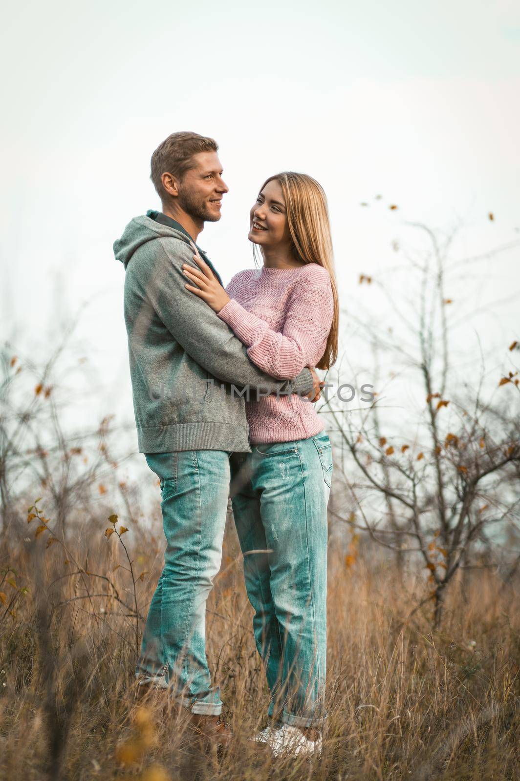 Romantic Couple In Love Stands Embracing On The Grass. Caucasian Man And Woman Dressed In Casual Are Walking In The Fresh Air Outdoors. Healthy Lifestyle Concept.