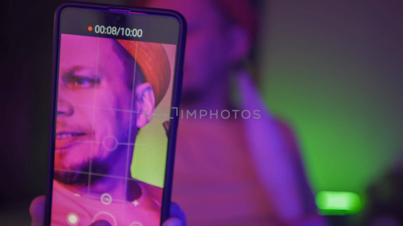 Man Making Streaming Videos By Phone In Neon Light by LipikStockMedia