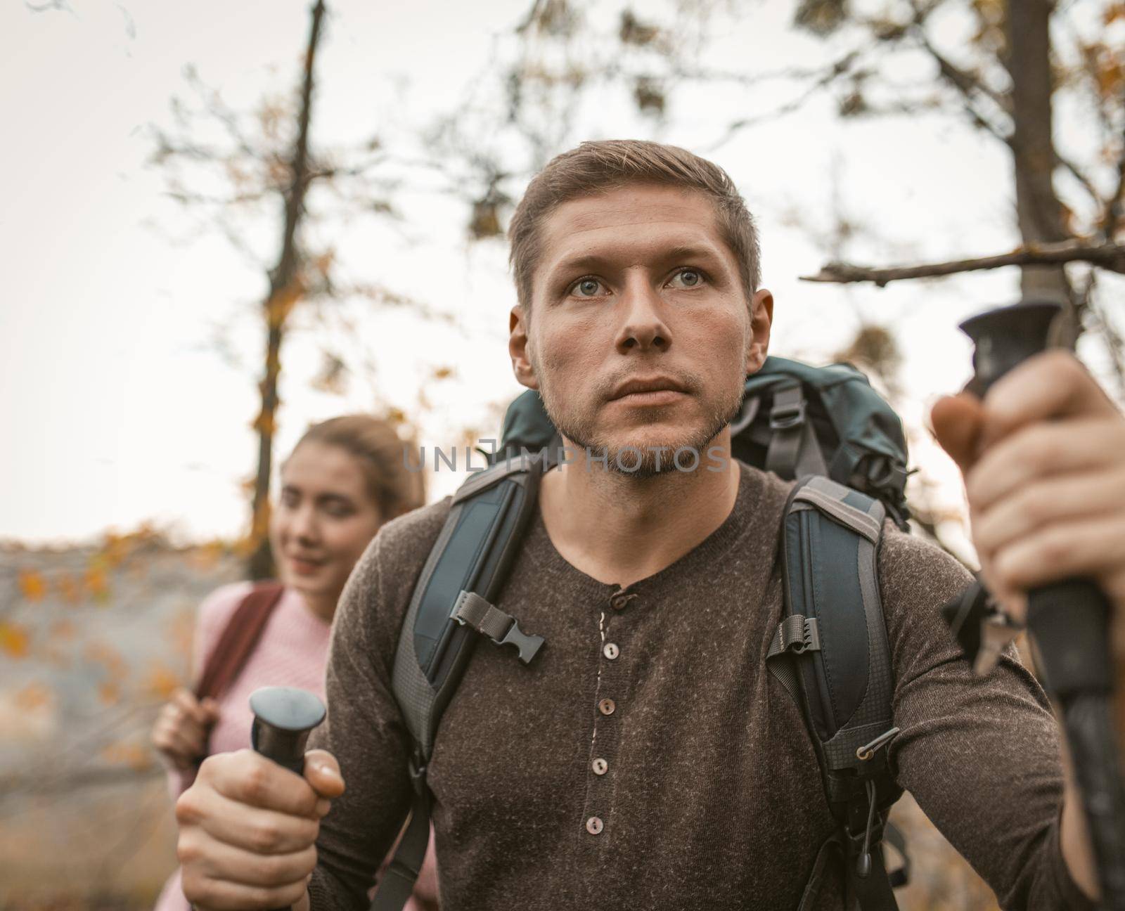 Man and a woman with backpacks walk together through the autumn forest, Selective focus on young man looking forward leaning on hiking pools. Family hiking Concept.