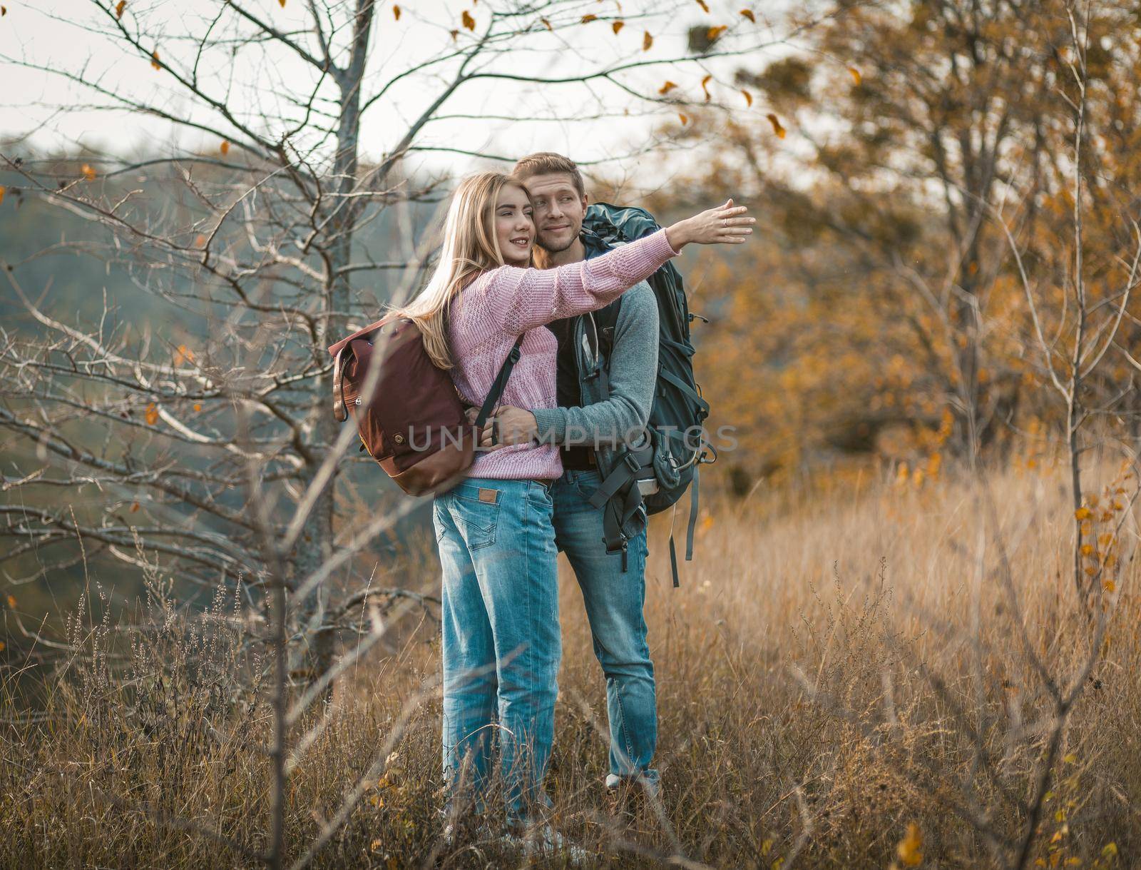 Tourists admire nature standing embracing. Selective focus on a charming Caucasian woman in a pink sweater pointing her hand into the distance. Hiking and travel concept by LipikStockMedia