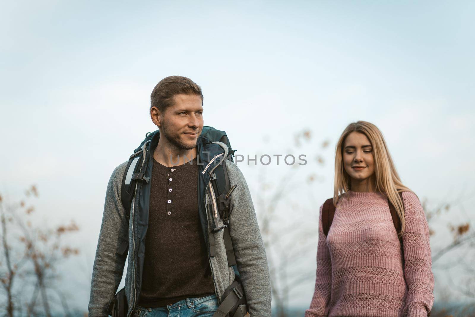 Young family leads a healthy lifestyle Walking in the fresh air, Couple of tourists are hiking on nature, focus on a smiling Caucasian man with a backpack in gray casual clothes