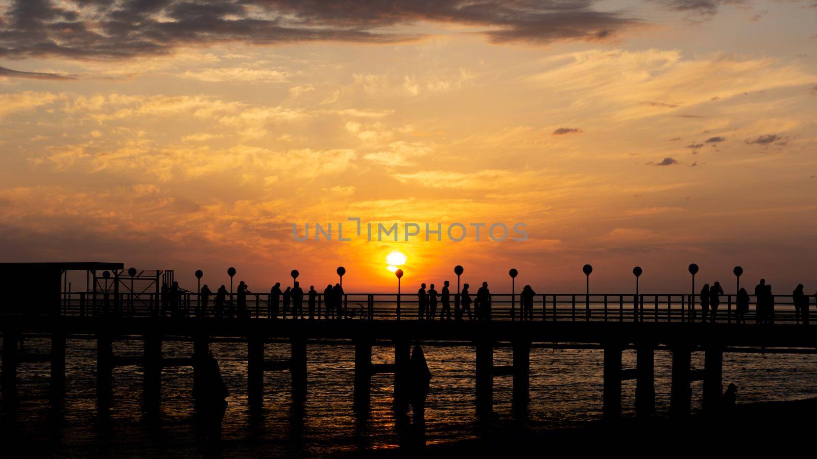 LAZAREVSKOE, SOCHI, RUSSIA - MAY, 26, 2021: Orange saturated sunset with silhouettes of people on the background of the sun.