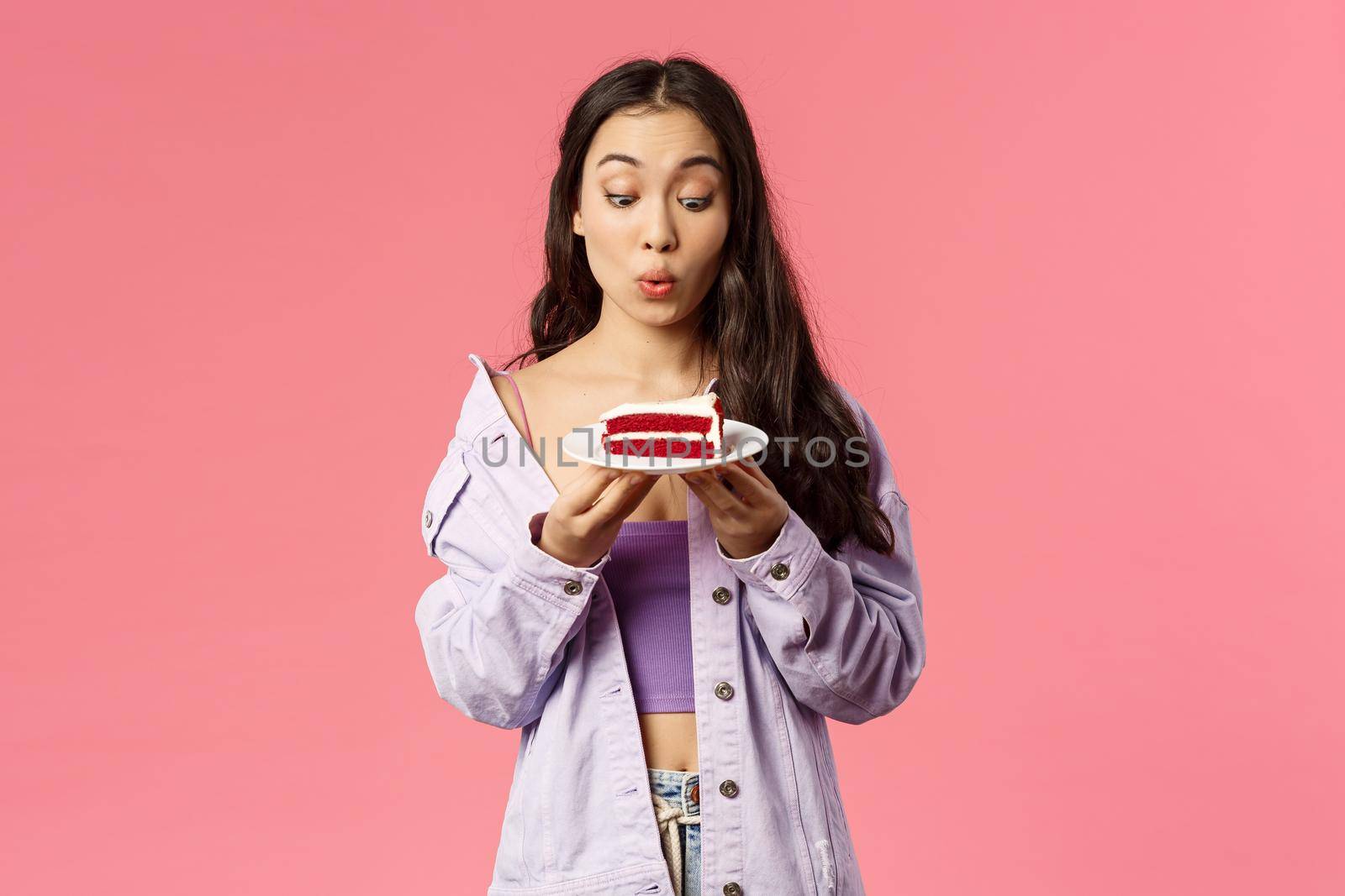 Portrait of excited and amused young pretty girl eager to have bite of this delicious dessert, looking happy and tempted at piece cake, folding lips, gonna eat this now, pink background.