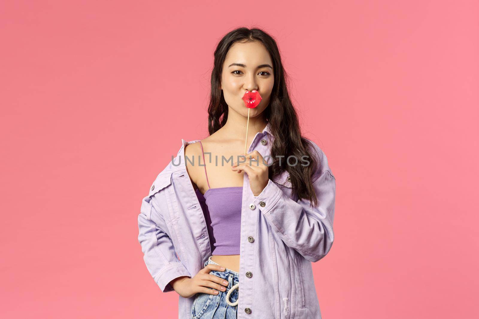 Holidays, lifestyle and people concept. Portrait of sassy attractive and stylish modern asian girl holding kissing lips stick and make confident expressing, showing her attitude, pink background.