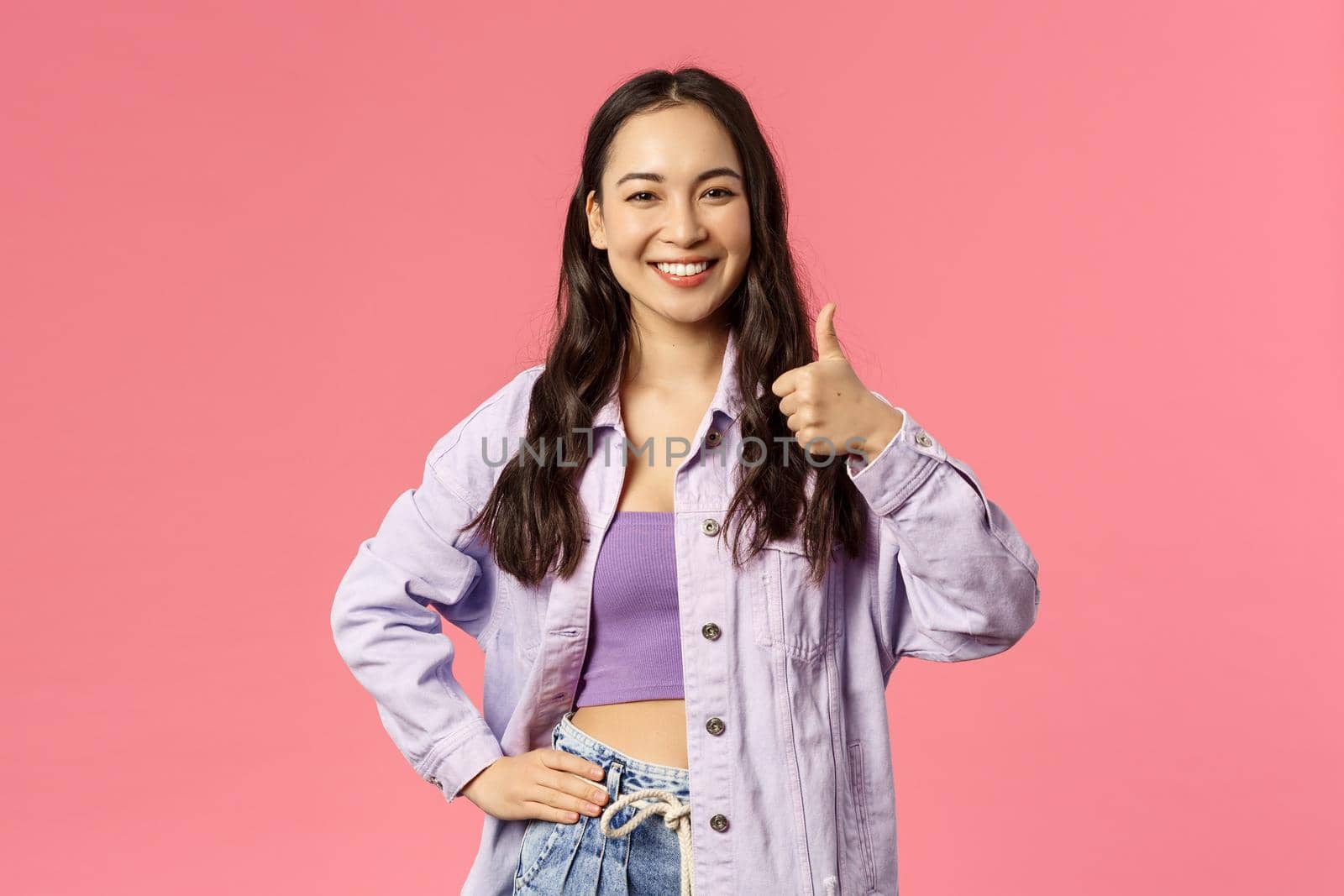 I am in. Cheerful confident pretty, stylish asian girl supports you, show thumb-up and smiling with approval, nod agree friend made good point, like and accept plan, pink background.