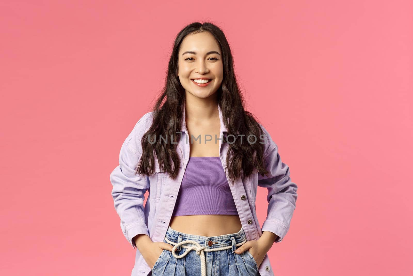 Portrait of cheerful, carefree smiling korean girl with happy pleased expression, hold hands in pockets, enjoying summer, having great plans, found excellent deal, online courses or product promo.