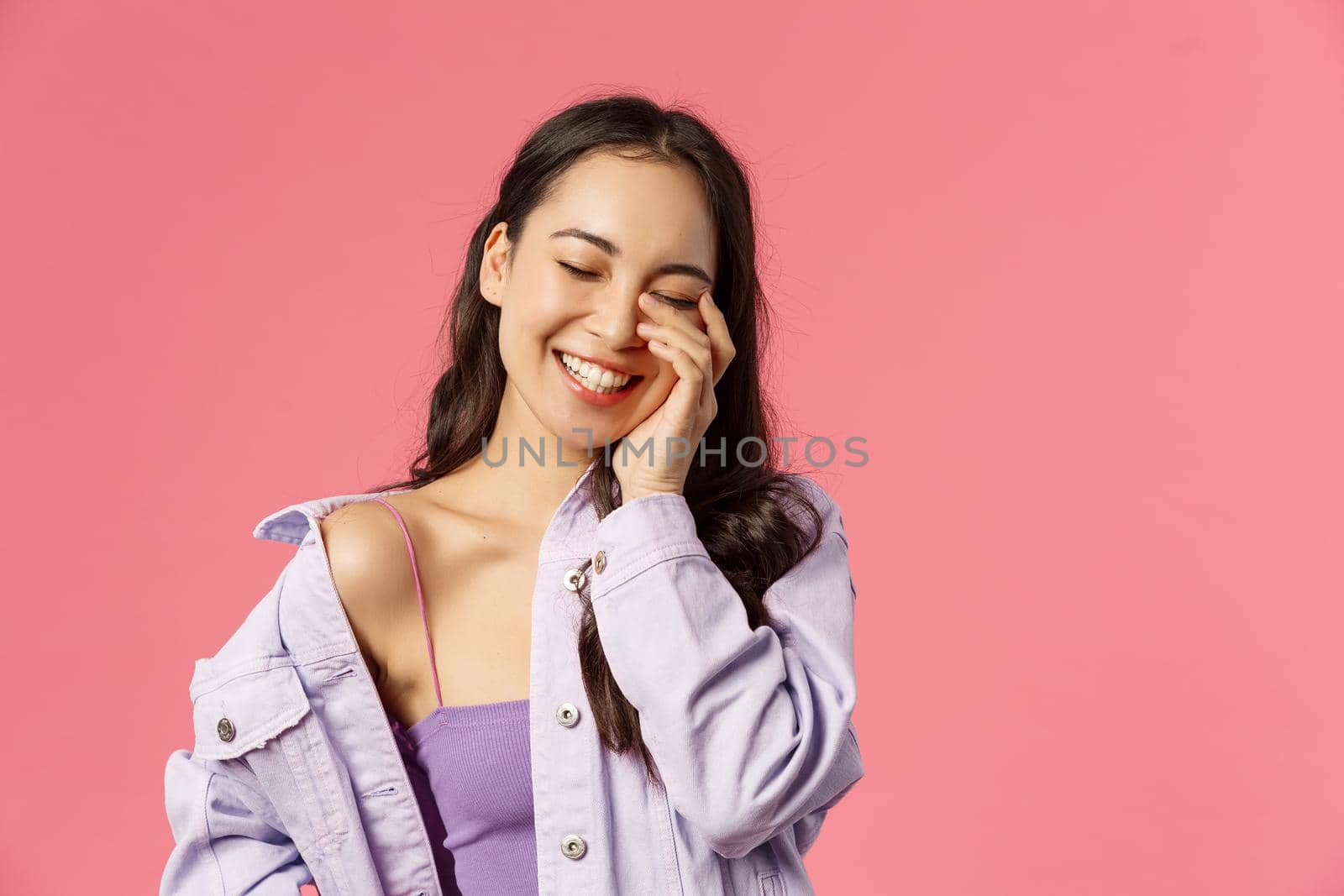 Lifestyle, fashion and beauty concept. Close-up portrait of laughing happy, attractive asian woman close eyes as giggle, touching face, communicating, express positive emotions, pink background.