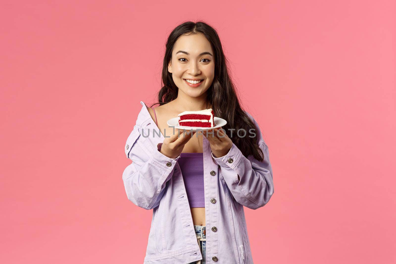 Got you some sweet dessert. Portrait of cheerful young asian girl holding piece of delicious cake, smiling happy, eating out at favorite cafe, standing pink background joyful.