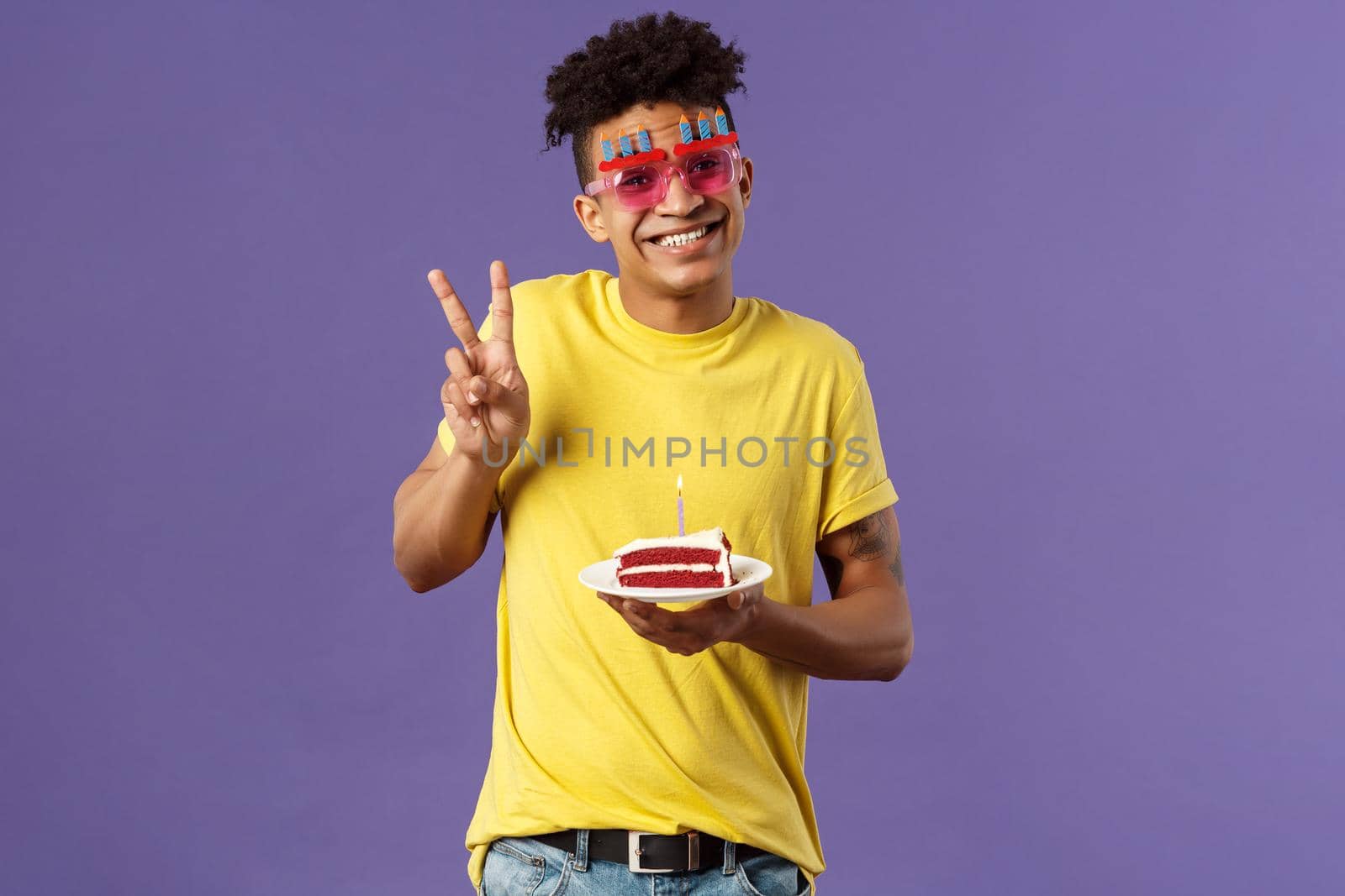 Celebration, party and holidays concept. Portrait of lovely charismatic hispaic guy in b-day glasses, celebrating his day, show peace sign photographing with birthday cake and lit candle, smiling.