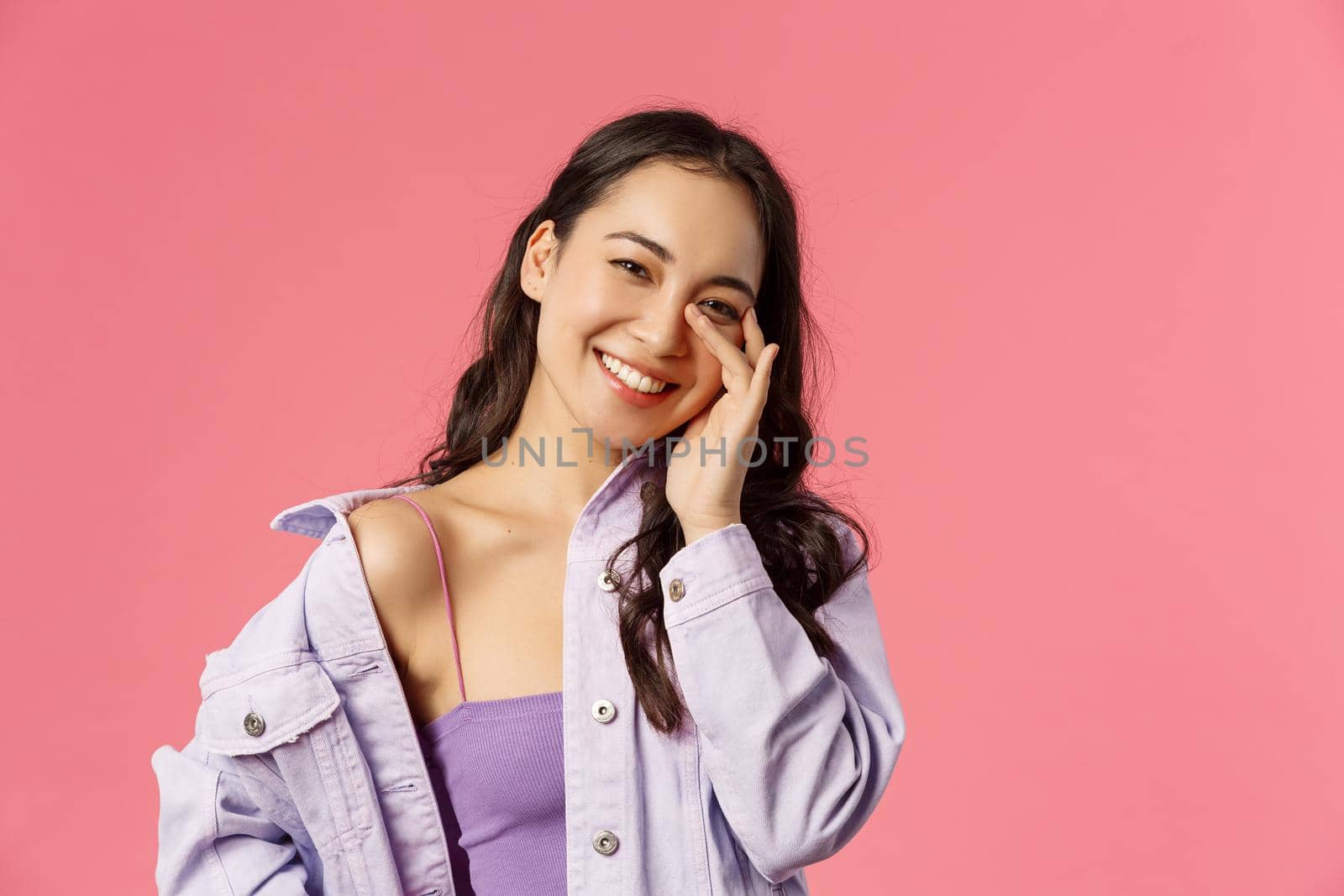 Lifestyle, fashion and beauty concept. Close-up portrait of carefree, smiling happy asian girl tilt head tender look camera, touching face, advertisement of skincare routine products, pink background by Benzoix