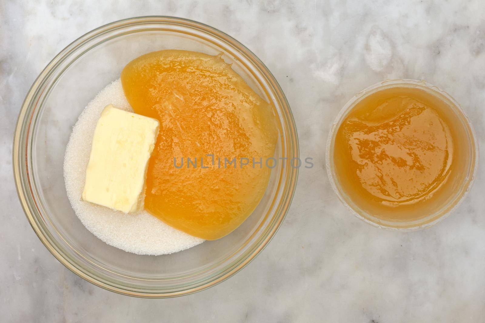 Top view of sugar honey and butter in glass bowl as ingredients of cake medovik on marble background