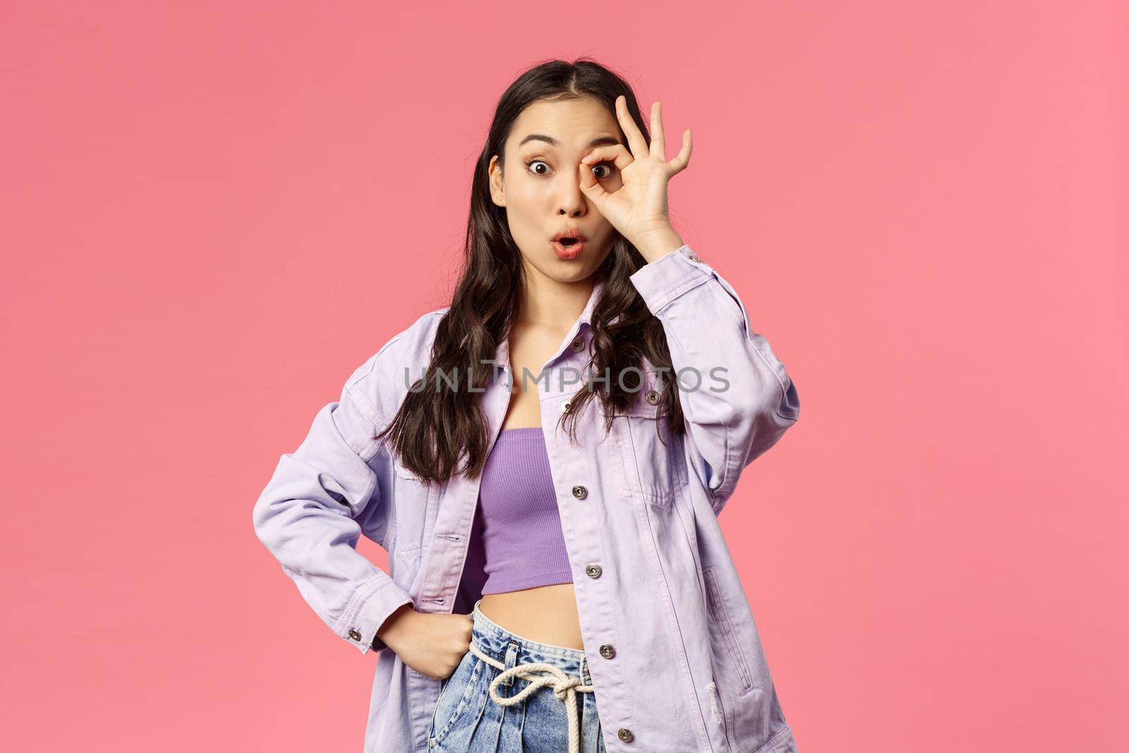 Portrait of surprised young woman seeing zero reasons not follow this page or buy product online shop, see something good, look through okay sign and fold lips say wow, pink background by Benzoix