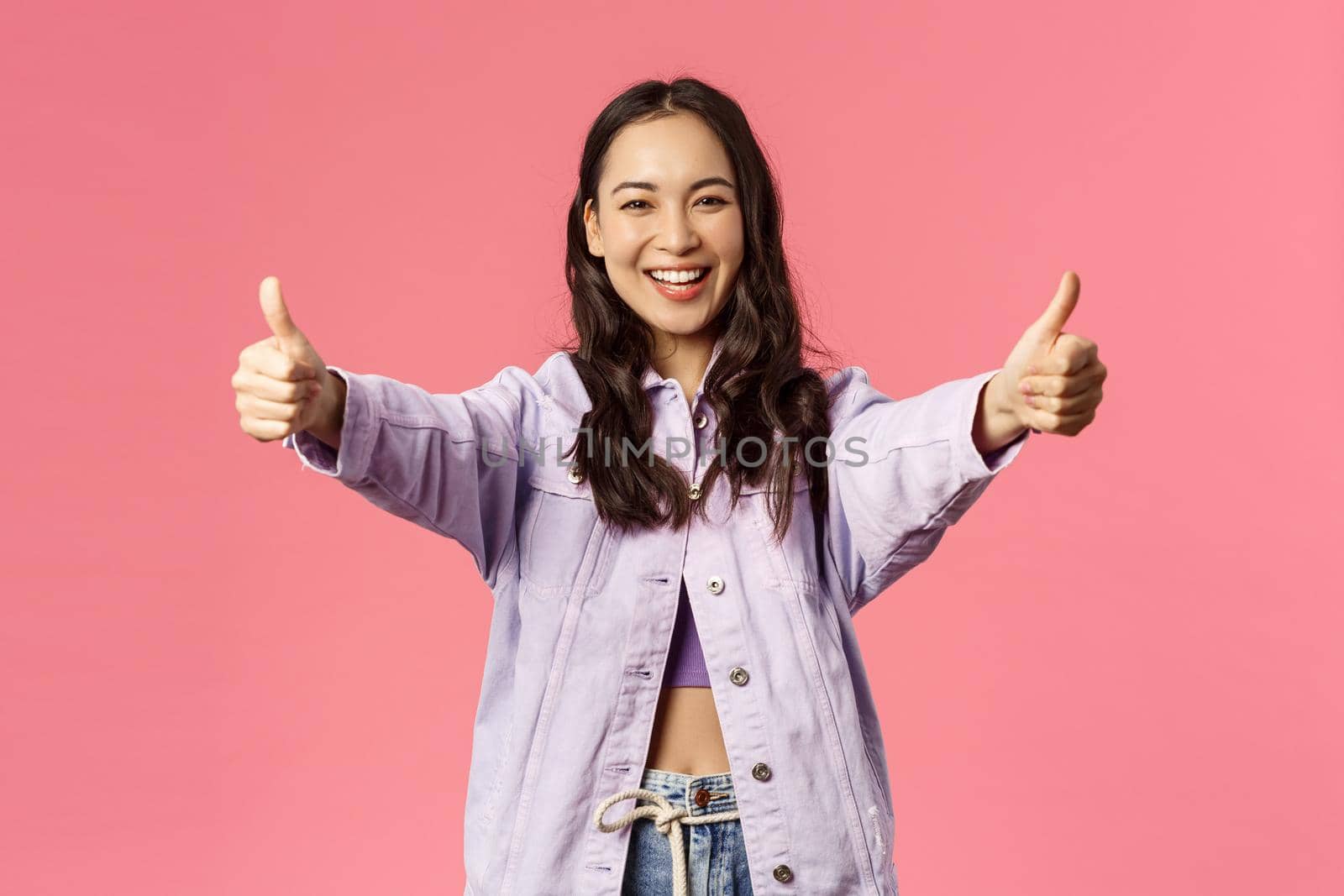 Totally agree. Portrait of cheerful young woman in denim jacket approve awesome, super cool idea, show thumbs-up and smiling happy, cheering, rooting or encourage do it, like plan, pink background by Benzoix