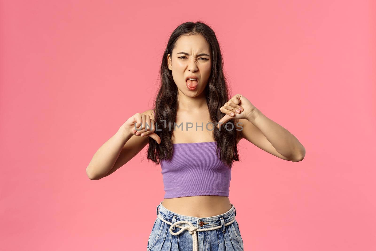 It was really bad. Portrait of disappointed young attractive woman tell friend her date wend awful, show thumbs-down and tongue, grimacing from aversion and dislike, disappointed, pink background.