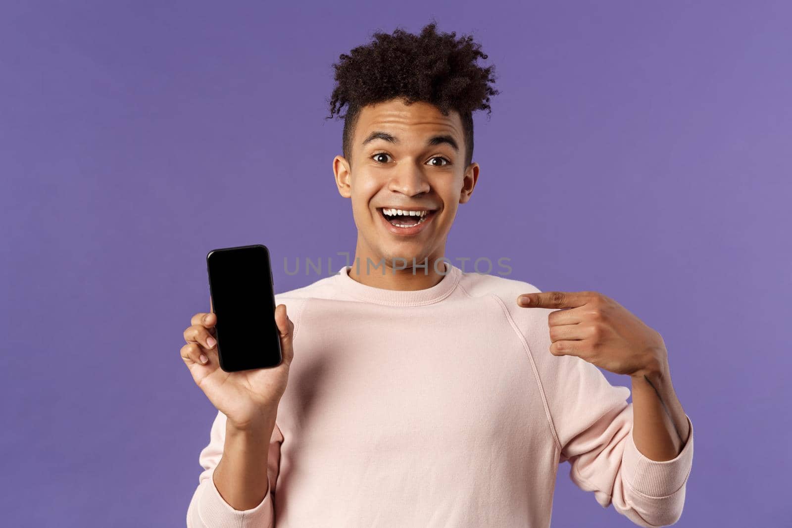 Portrait of excited, happy smiling man talking about new application or game feature, pointing at smartphone display, talking about mobile phone with amused cheerful expression by Benzoix