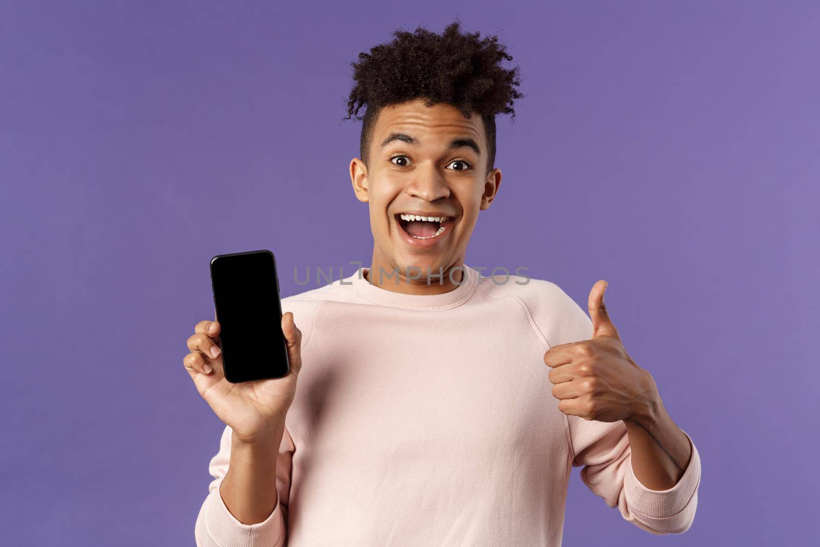 Happy young man, hispanic guy with dreads recommend app, online delivery service or food order, show thumbs-up, smiling excited, holding mobile phone, show smartphone screen.