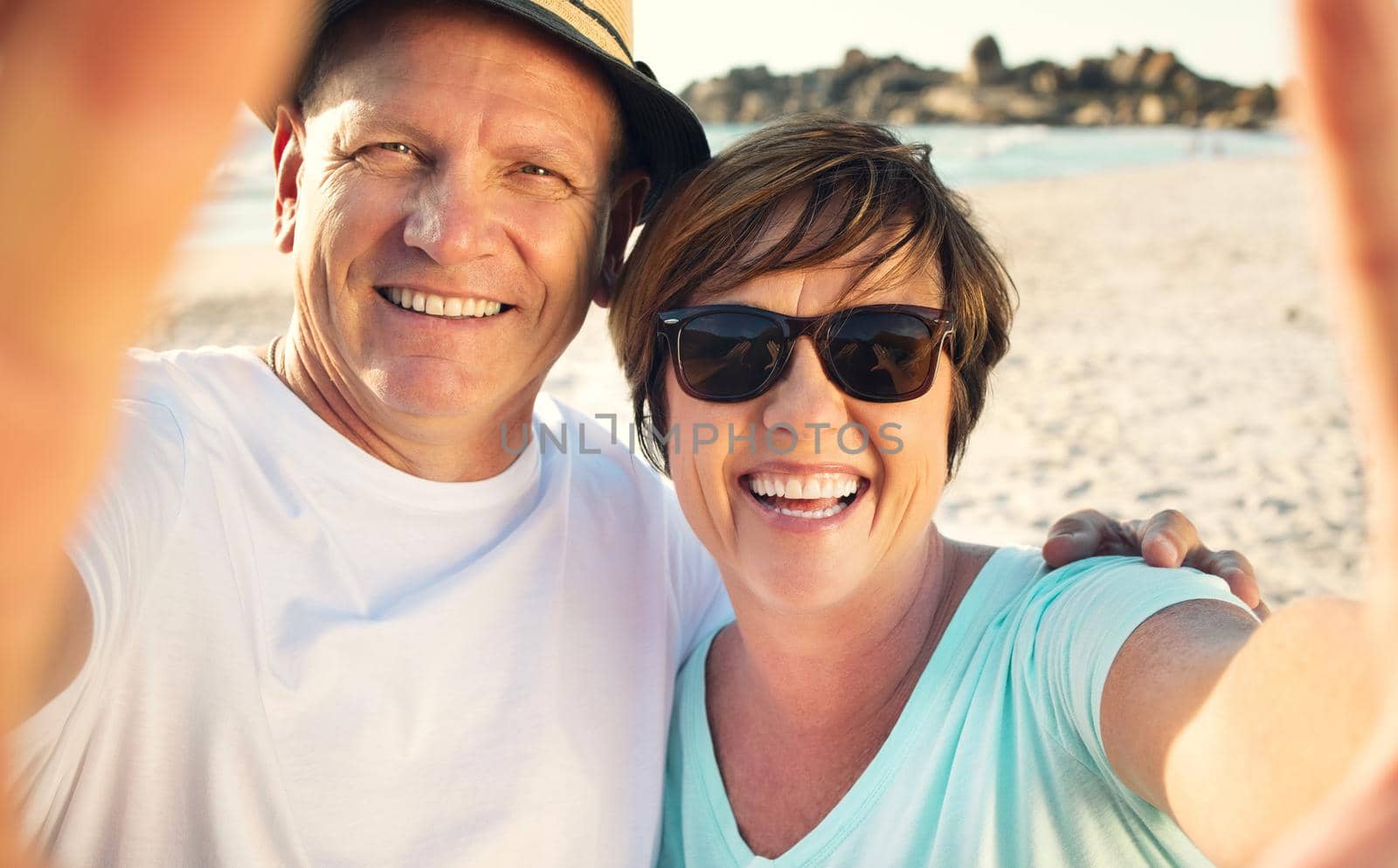 We enjoying our vacation and want to share it with our family. a mature couple taking a selfie while spending the day at the beach