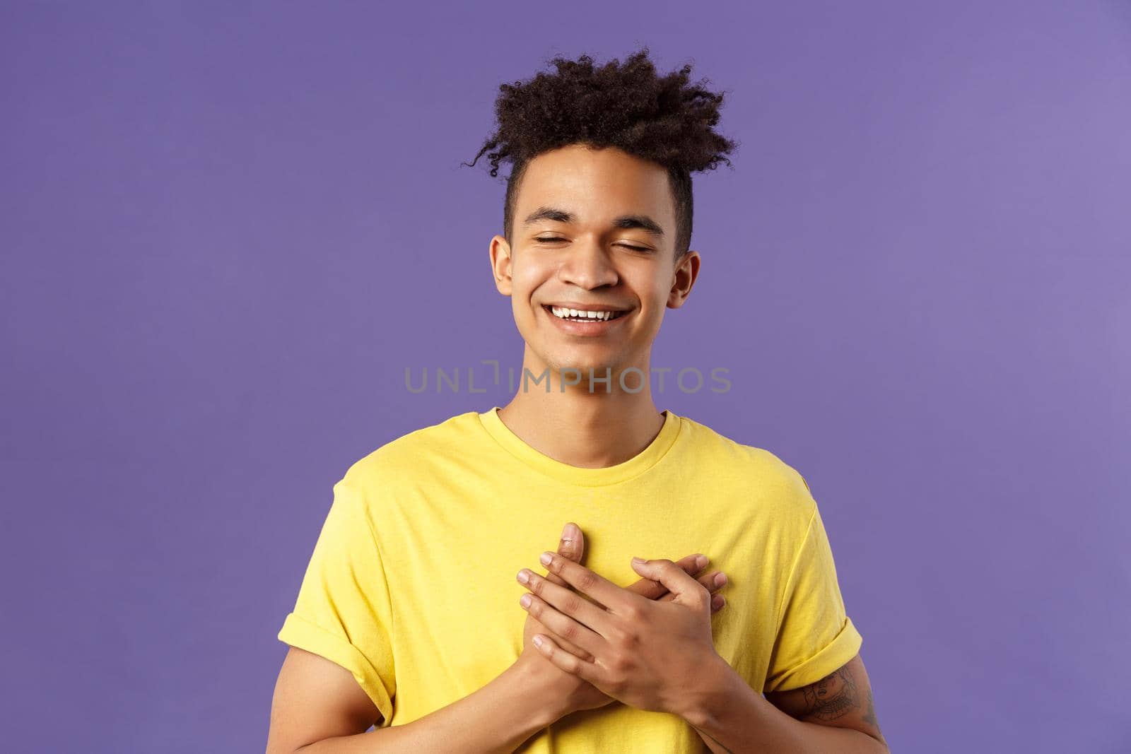 Close-up portrait of happy, upbeat young dreamy guy, remember sweet memories, hold hands on heart, smiling touched and delighted, close eyes grinning, recall romantic moment.
