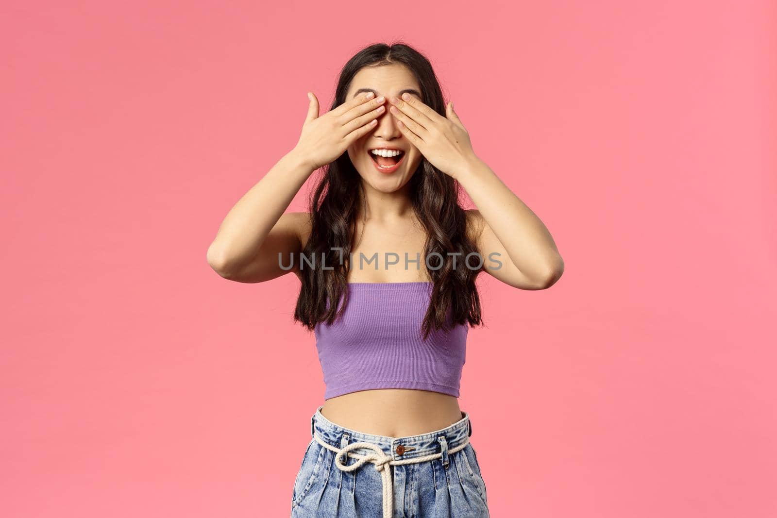 Portrait of excited enthusiastic good-looking woman in crop-top, awaiting for command to open eyes, smiling amused, blindfolded waiting surprise gift, standing pink background by Benzoix