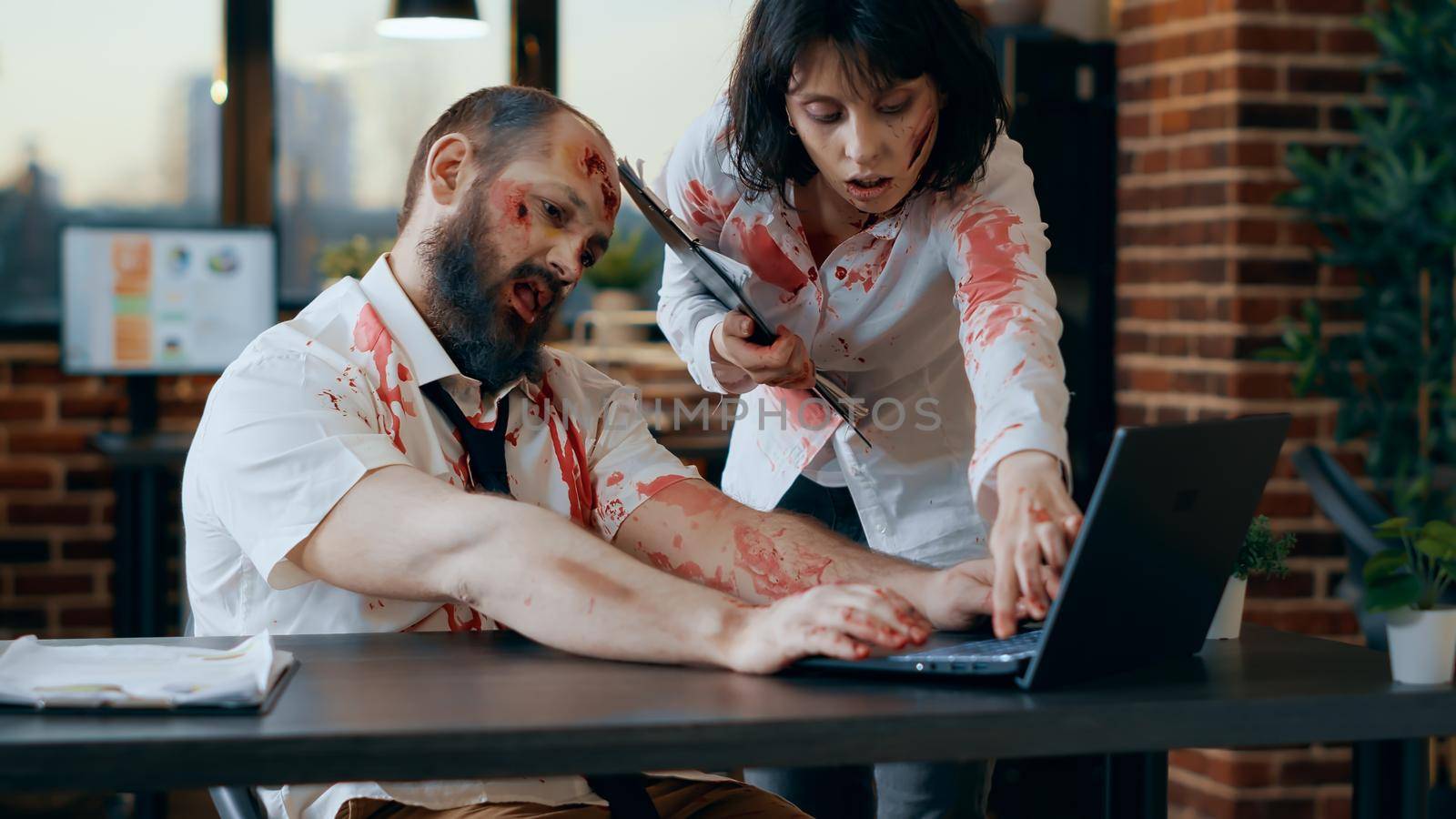 Creepy looking office zombie working on laptop while smirking bizarre at camera. Dangerous brain dead monster with bloody and deep scars and wounds trying to use computer but fails.