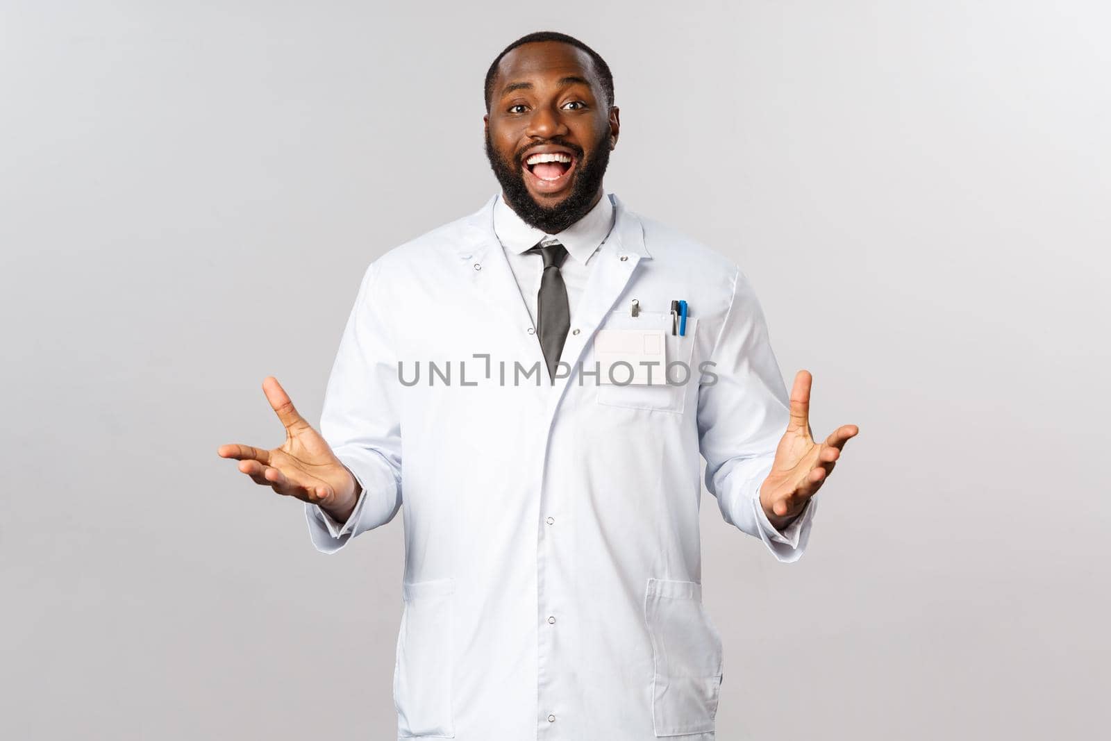 Happy african american doctor at clinic or hospital welcoming patient, telling good news to family after treating person from covid19 severe sympthoms, gesturing and smiling, wear white coat.