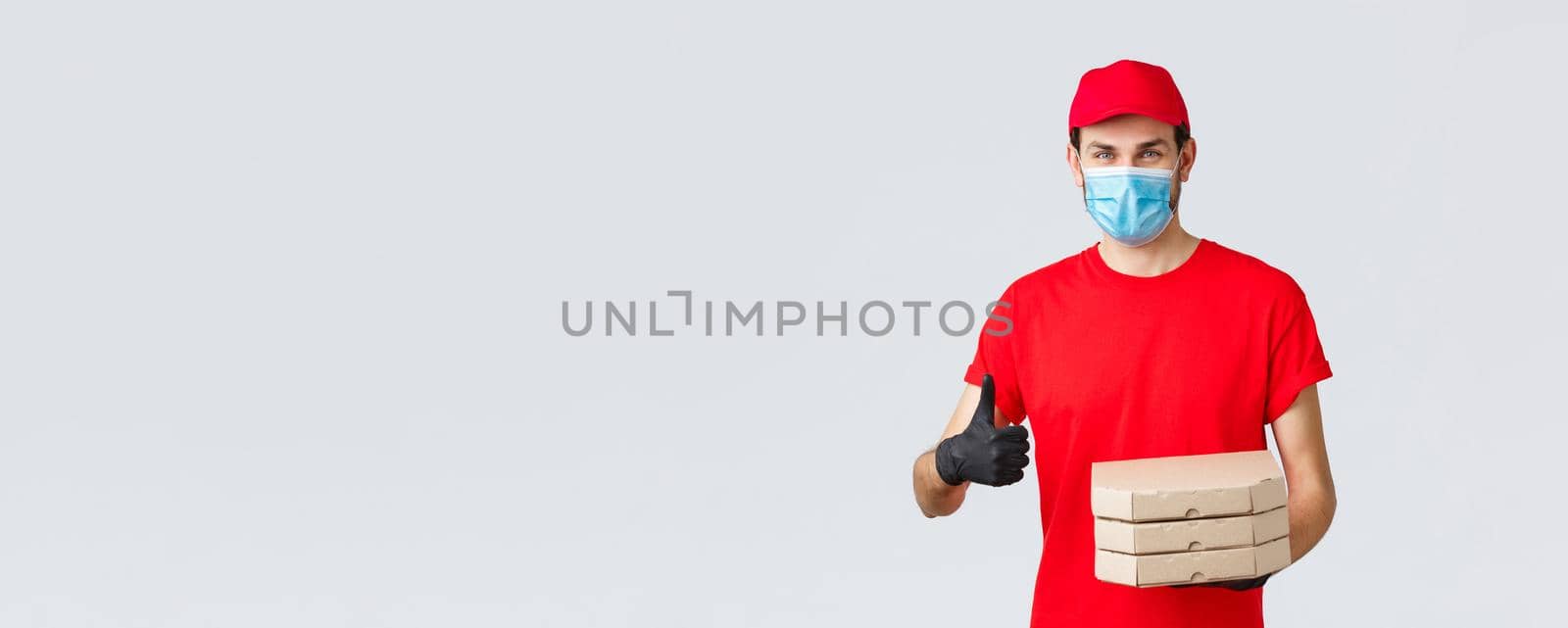 Food delivery, application, online grocery, contactless shopping and covid-19 concept. Smiling caucasian courier in red uniform, gloves and face mask, provide best offers, pizza express delivery.