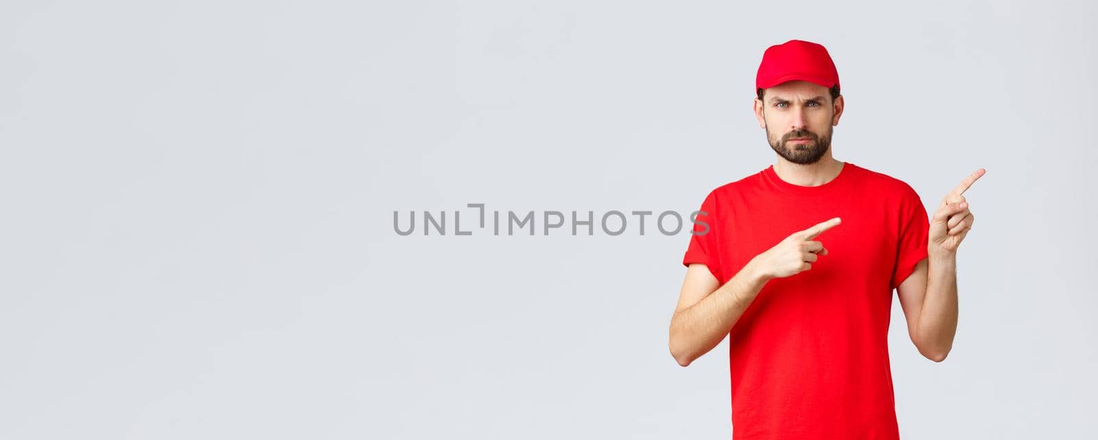 Online shopping, delivery during quarantine and takeaway concept. Displeased angry courier in red uniform cap and t-shirt, frowning grumpy, pointing fingers right in disapproval, feel bothered by Benzoix