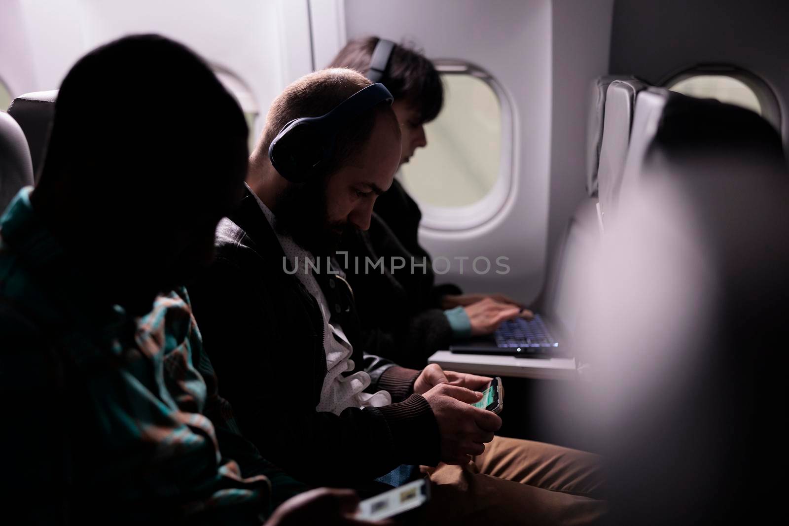 Diverse tourists flying in economy class with airplane, travelling on business work trip or holiday destination. Using laptop and phone on plane flight, fly international airways.
