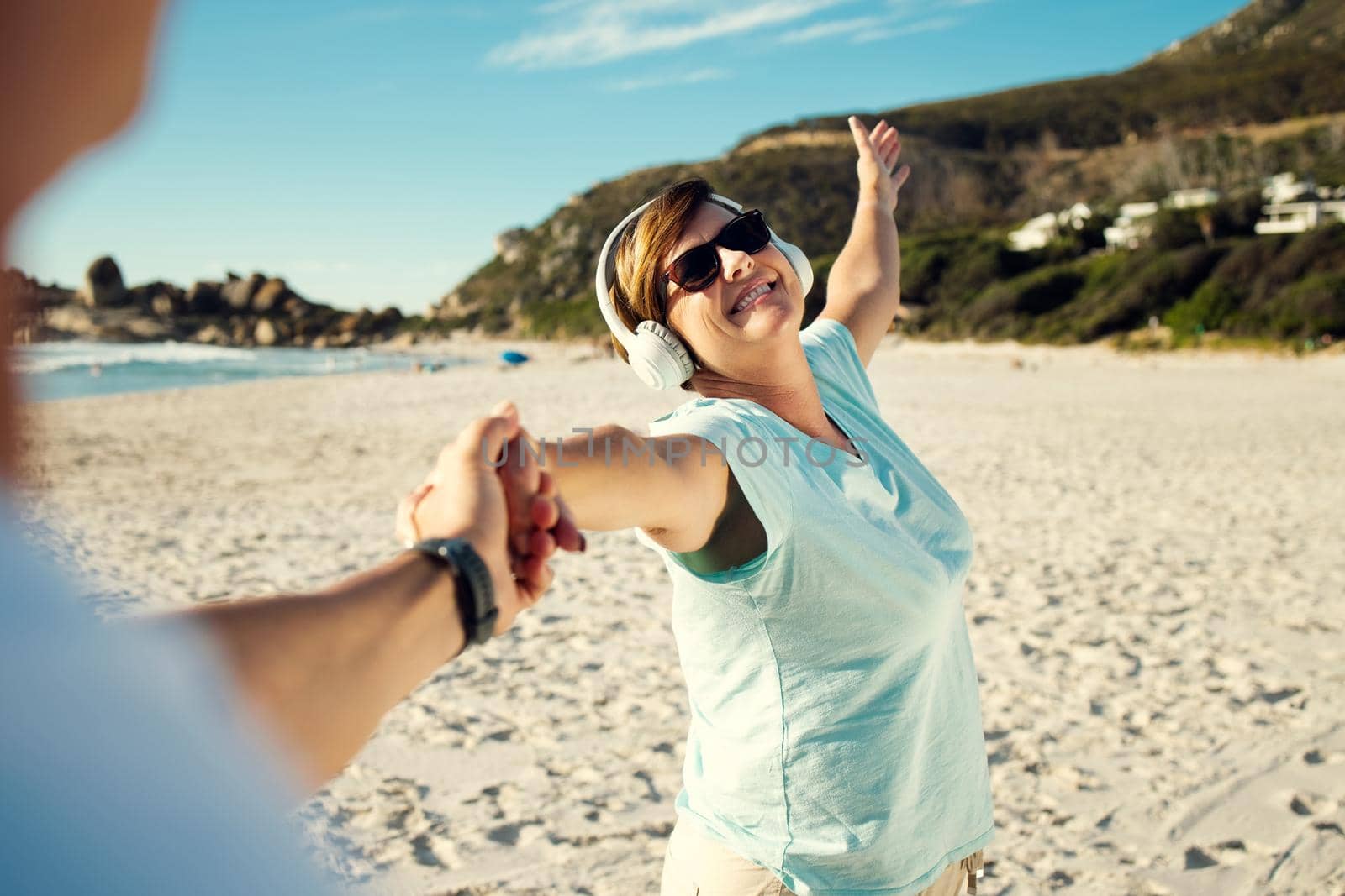 Now is the time to live your best life. a woman wearing headphones and enjoying herself at the beach. by YuriArcurs