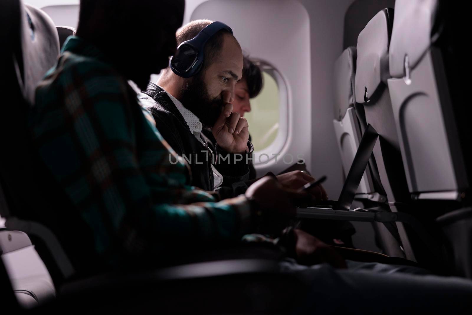 Diverse group of travellers flying abroad by airplane jet, using modern devices during international plane transportation. Travelling in economy class with airways flight trip.