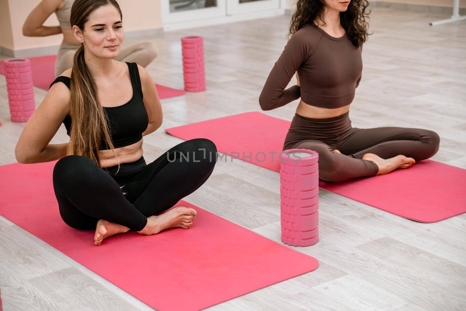 A group of six athletic women doing pilates or yoga on pink mats in front of a window in a beige loft studio interior. Teamwork, good mood and healthy lifestyle concept. by Matiunina