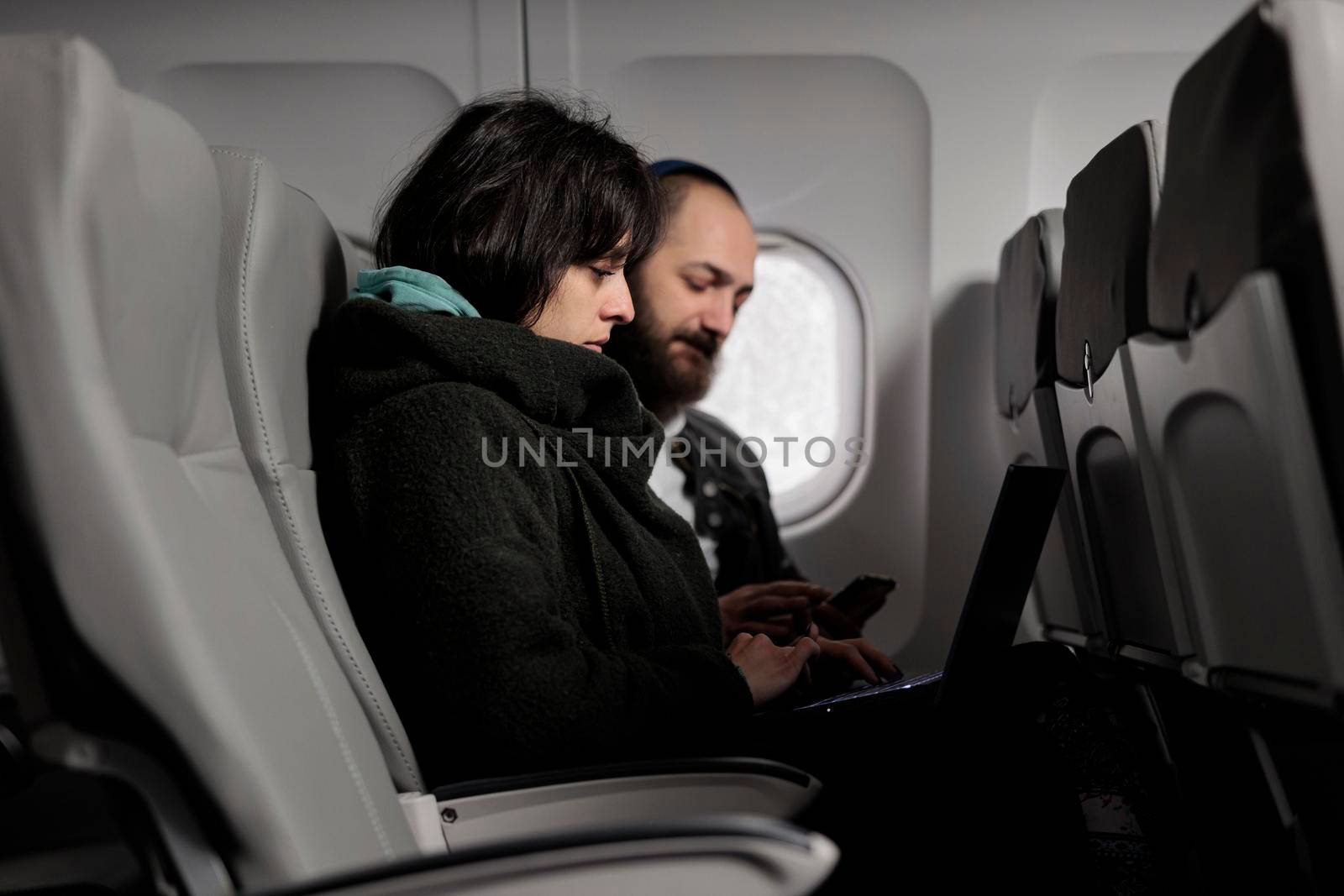 Young people travelling on holiday trip with aerial transportation, using laptop with online internet on commercial flight. Man and woman browsing computer on holiday destination, flying with plane.