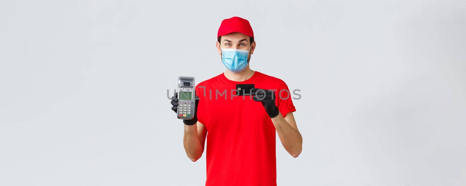 Contactless delivery, payment and online shopping during covid-19, self-quarantine. Handsome courier with paying terminal POS and credit card, provide safe pay order, wear face mask and gloves by Benzoix