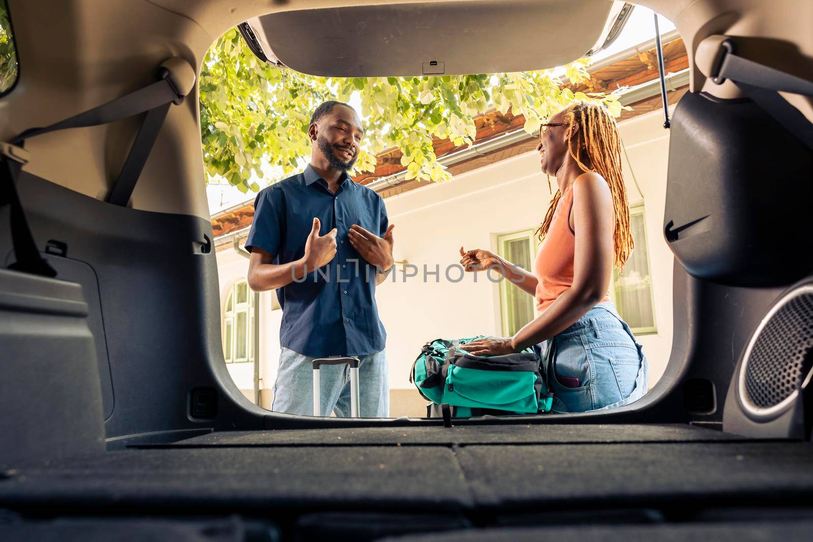 African american couple putting travel bags and trolley in trunk, getting ready to leave on holiday vacation with automobile. Travelling by car on road trip with luggage and suitcases.