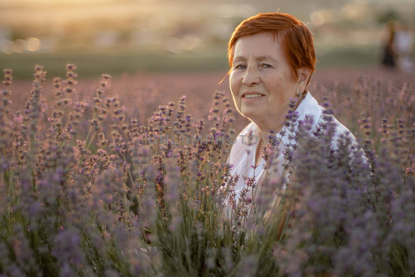 A middle-aged woman sits in a lavender field and enjoys aromatherapy. Aromatherapy concept, lavender oil, photo session in lavender by Matiunina